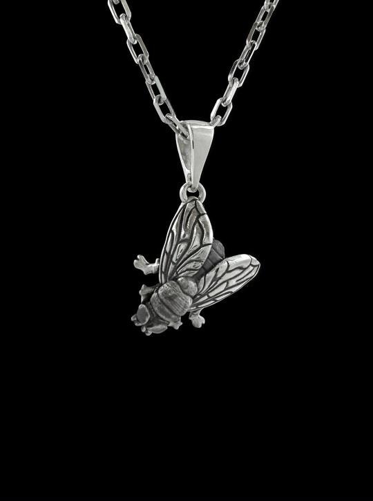 May include: A silver-colored pendant necklace featuring a detailed insect design. The pendant depicts a cicada with intricate wing and body details, suspended from a delicate chain. The necklace is displayed against a white background.