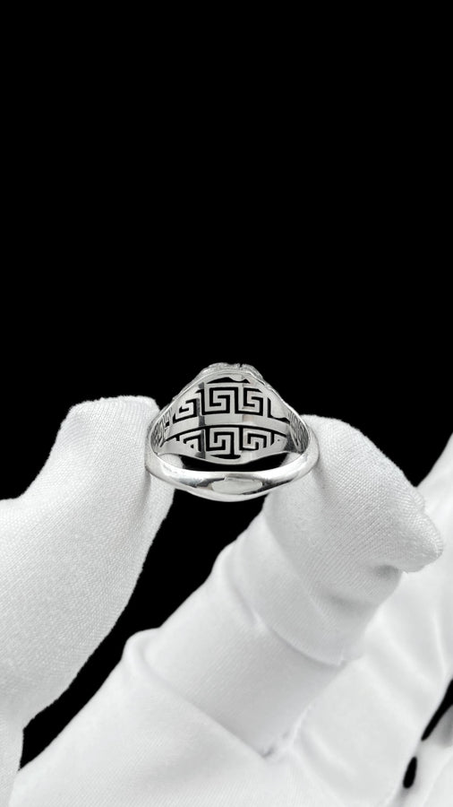 A high-contrast macro photograph of a heavy sterling silver ring resting against a pitch-black background. The ring features a three-dimensional sculpture of a classical Greek goddess's face, likely Athena. A jagged, deep crack splits the face vertically. The right side shows smooth, classical features, while the left side transitions into a rough, eroded, and porous texture resembling crumbling ancient stone. The silver is heavily oxidized t (etsy image id: 7831406732)