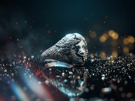 A high-contrast macro photograph of a heavy sterling silver ring resting against a pitch-black background. The ring features a three-dimensional sculpture of a classical Greek goddess's face, likely Athena. A jagged, deep crack splits the face vertically. The right side shows smooth, classical features, while the left side transitions into a rough, eroded, and porous texture resembling crumbling ancient stone. The silver is heavily oxidized t (etsy image id: 7831406732)
