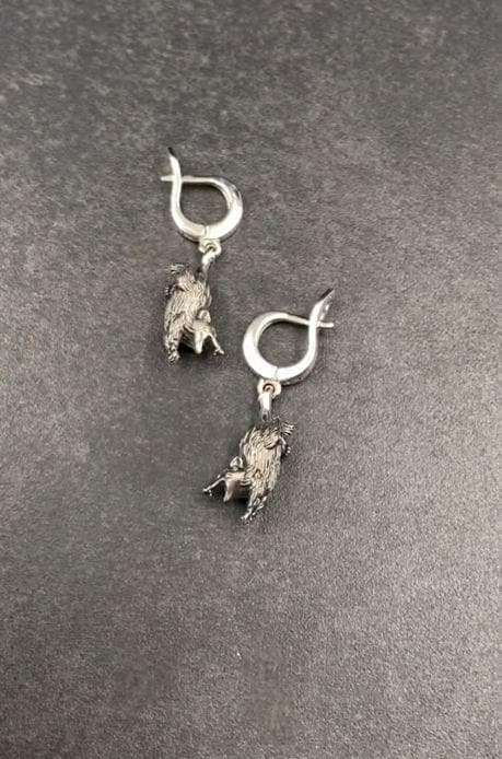 A close-up studio shot of sterling silver dangle earrings featuring detailed opossums. The animals are depicted with open mouths and textured fur, hanging from polished lever-back clasps. The metal is heavily oxidized in the recesses to enhance the realistic, rugged appearance of the marsupials against a white fabric background.