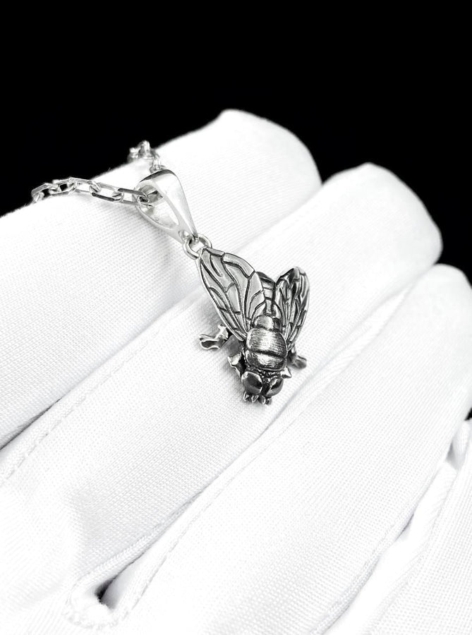 May include: A silver-colored pendant necklace featuring a detailed insect design. The pendant depicts a cicada with intricate wing and body details, suspended from a delicate chain. The necklace is displayed against a white background.