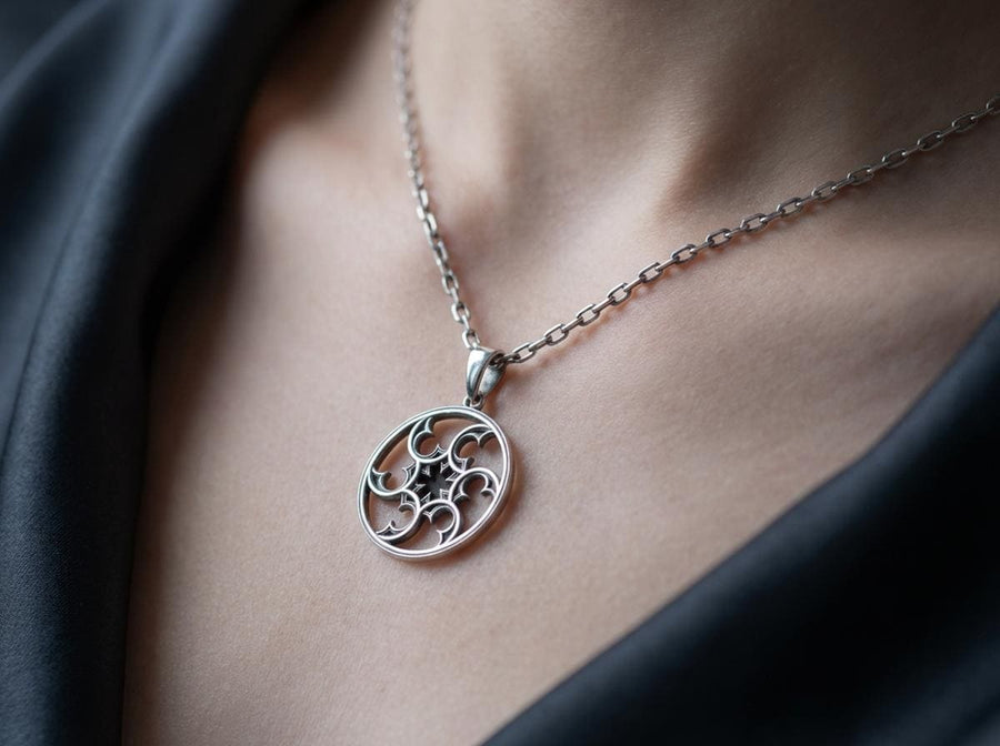 A detailed close-up of a circular sterling silver pendant resting on a dark blue, textured silk fabric. The pendant features an openwork design with swirling, crescent-like shapes radiating from a central four-pointed star. The intricate pattern resembles a gothic rose window or a celestial wheel. The raised metal surfaces are polished to a bright silver shine, contrasting beautifully against the dark, oxidized background recesses. (etsy image id: 7830974908)