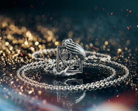 A close-up studio photograph of a highly detailed sterling silver pendant resting on a luxurious, dark blue silk fabric with silvery thread patterns. The pendant's striking design features two realistically sculpted, three-dimensional hands emerging from the sides to gently grasp a rectangular Gothic window frame. Inside the frame sits intricate openwork tracery, forming a classic quatrefoil motif. The polished silver highlights contrast with (etsy image id: 7879251833)