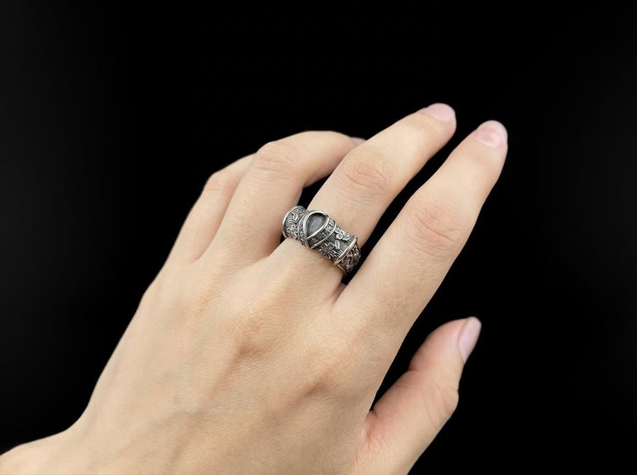 A close-up studio photograph of a wide sterling silver ring designed to look like folded fabric. The overlapping top mimics an Obi, the traditional Japanese kimono sash. The band features highly detailed relief carvings of Sakura (cherry blossoms) and Seigaiha (concentric ocean waves) patterns. A raised ribbon section bears engraved Japanese Kanji script. The silver is heavily oxidized in the recesses to highlight the intricate textures against t (etsy image id: 7831393878)