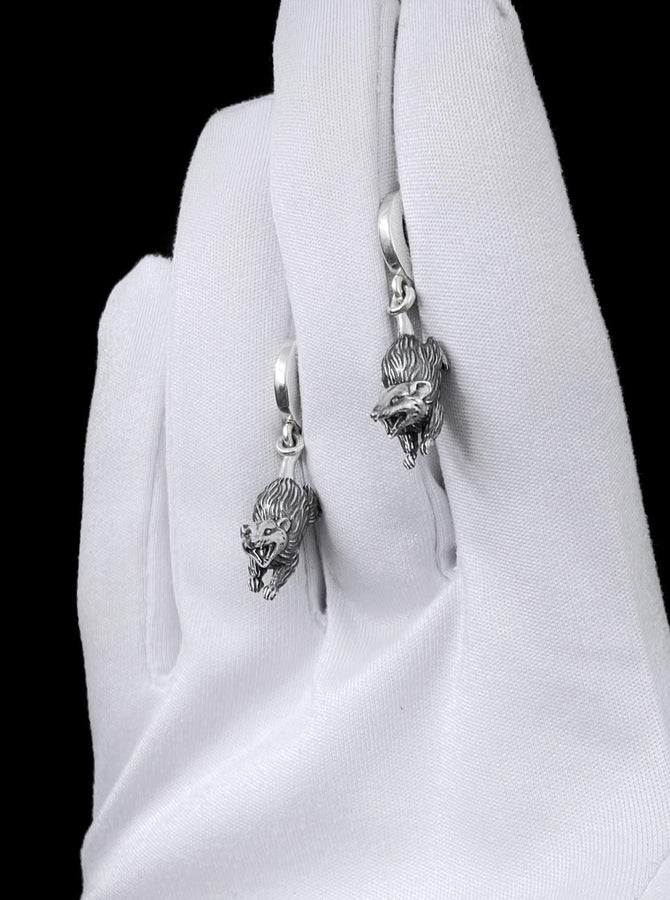 A close-up studio shot of sterling silver dangle earrings featuring detailed opossums. The animals are depicted with open mouths and textured fur, hanging from polished lever-back clasps. The metal is heavily oxidized in the recesses to enhance the realistic, rugged appearance of the marsupials against a white fabric background.