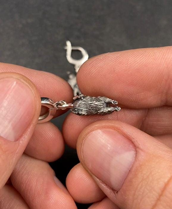 A close-up studio shot of sterling silver dangle earrings featuring detailed opossums. The animals are depicted with open mouths and textured fur, hanging from polished lever-back clasps. The metal is heavily oxidized in the recesses to enhance the realistic, rugged appearance of the marsupials against a white fabric background.