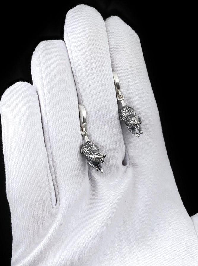 A close-up studio shot of sterling silver dangle earrings featuring detailed opossums. The animals are depicted with open mouths and textured fur, hanging from polished lever-back clasps. The metal is heavily oxidized in the recesses to enhance the realistic, rugged appearance of the marsupials against a white fabric background.