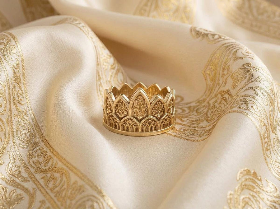 A close-up studio shot of a wide sterling silver ring resting on a dark patterned brocade fabric. The band features a majestic crown or tiara silhouette made of continuous pointed gothic arches. Inside each arch is delicate, openwork filigree that resembles the ornamental stone latticework of cathedral windows. The silver is oxidized in the recesses to highlight the raised, polished metal. (etsy image id: 7910304990)