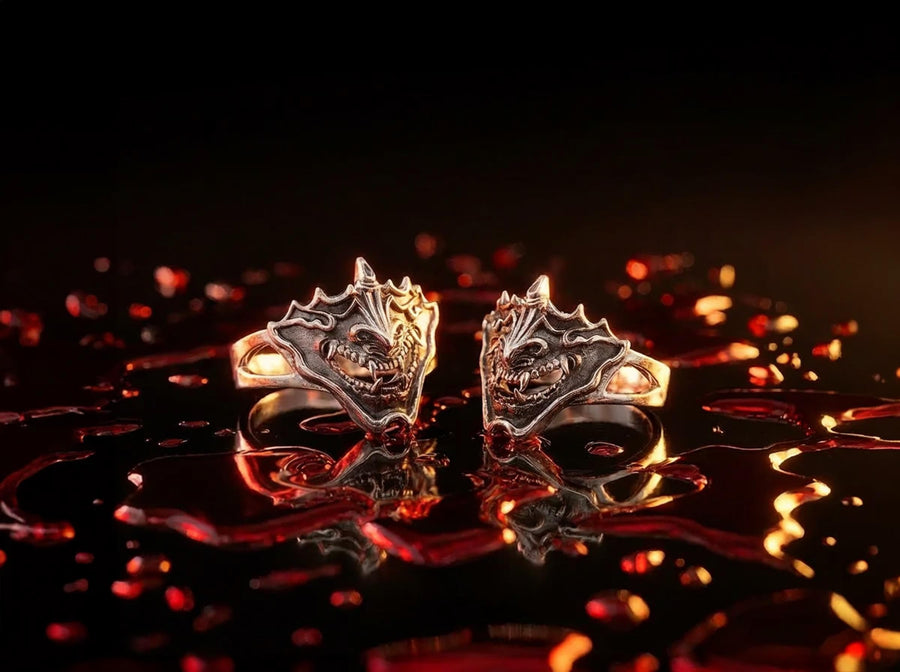 A close-up studio shot of a sterling silver ring featuring a detailed Japanese Oni mask. The demon face has sharp fangs, a wide menacing grin, and two distinct horns protruding from its forehead. The band features openwork cutouts on the sides, merging seamlessly with the mask. The metal is heavily oxidized to a dark charcoal in the recesses, making the highly polished silver ridges of the fierce expression pop against the dark reflective backgro (etsy image id: 7959798327)