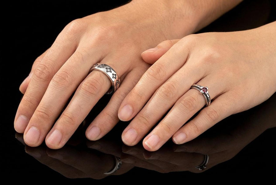 A high-resolution studio shot of a matching sterling silver gothic wedding ring set resting on a sparkling, white surface scattered with tiny crystals. The beautiful set includes a wide men's band and a narrower engagement ring centering a vibrant round red ruby. Both rings feature precisely polished medieval quatrefoil motifs four-lobed geometric shapes set against a deeply oxidized, stippled dark grey background, beautifully highlighting th