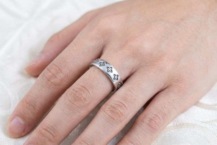 A high-resolution studio shot of a matching sterling silver gothic wedding ring set resting on a sparkling, white surface scattered with tiny crystals. The beautiful set includes a wide men's band and a narrower engagement ring centering a vibrant round red ruby. Both rings feature precisely polished medieval quatrefoil motifs four-lobed geometric shapes set against a deeply oxidized, stippled dark grey background, beautifully highlighting th