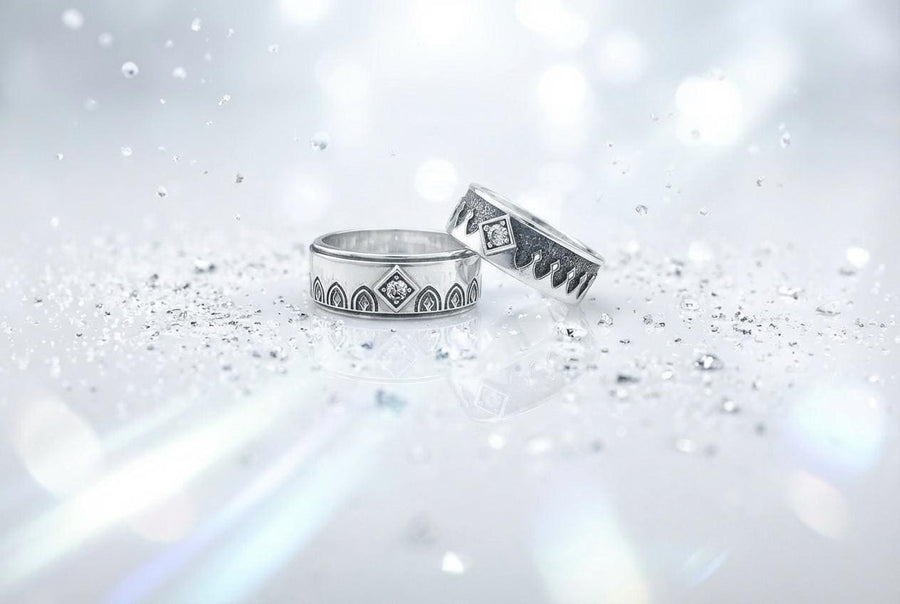 A high-resolution macro photograph of a matching sterling silver gothic wedding ring set resting on softly draped, luxurious white satin. The set features a wider masculine band and a slightly narrower feminine band. Both rings display a continuous engraved arcade of pointed medieval arches along the bottom edge, centering on a polished geometric rhombus frame that holds a brilliant round white gemstone. The polished silver beautifully contrasts