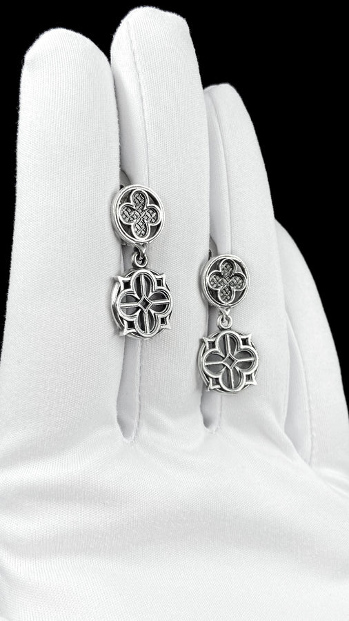 The image highlights the specific textures of the casting. The top stud has a "waffle" or lattice texture inside the quatrefoil lobes, mimicking chainmail or stone carving. The bottom drop is smooth and open, providing a visual counterweight. The 925 sterling silver is treated with an antique patina to enhance the "old world" feel. Modeled as a versatile daily earring, the "coin" size is modest enough for office wear (etsy image id: 5775868859)