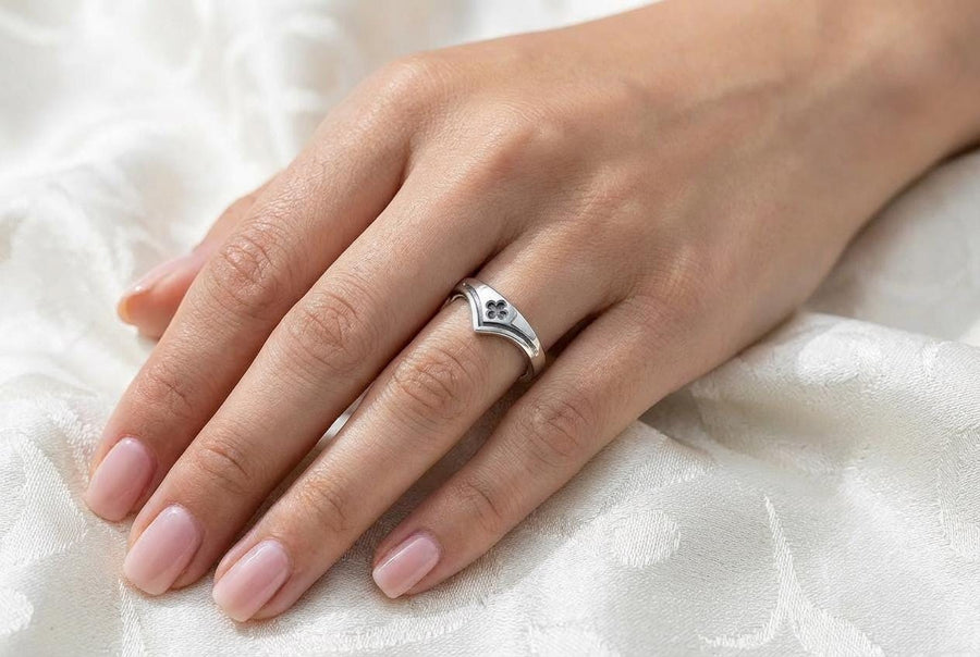 A high-resolution studio shot of a matching sterling silver wedding ring set resting on a sparkling, icy white surface. The set includes a wide unisex band and a delicate, V-shaped chevron ring. Both feature polished medieval quatrefoil motifs—four-lobed geometric shapes—set against a deeply textured, oxidized dark grey background that resembles crushed stone or stippled concrete.