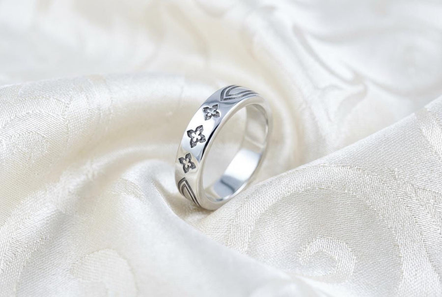 A high-resolution studio shot of a matching sterling silver gothic wedding ring set resting on a sparkling, white surface scattered with tiny crystals. The beautiful set includes a wide men's band and a narrower engagement ring centering a vibrant round red ruby. Both rings feature precisely polished medieval quatrefoil motifs four-lobed geometric shapes set against a deeply oxidized, stippled dark grey background, beautifully highlighting th
