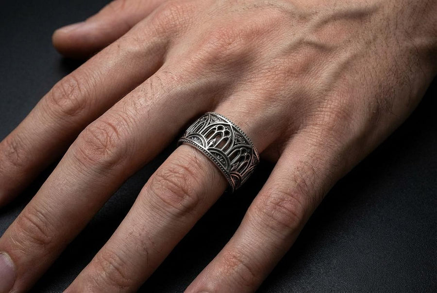 A high-resolution macro shot of a wide sterling silver wedding band resting on a sparkling, icy white surface. The ring features an intricate openwork design mimicking a Gothic cathedral window, complete with pointed lancet arches and delicate stone tracery. The polished silver highlights contrast beautifully against the dark, oxidized background, emphasizing the architectural depth of the piece.