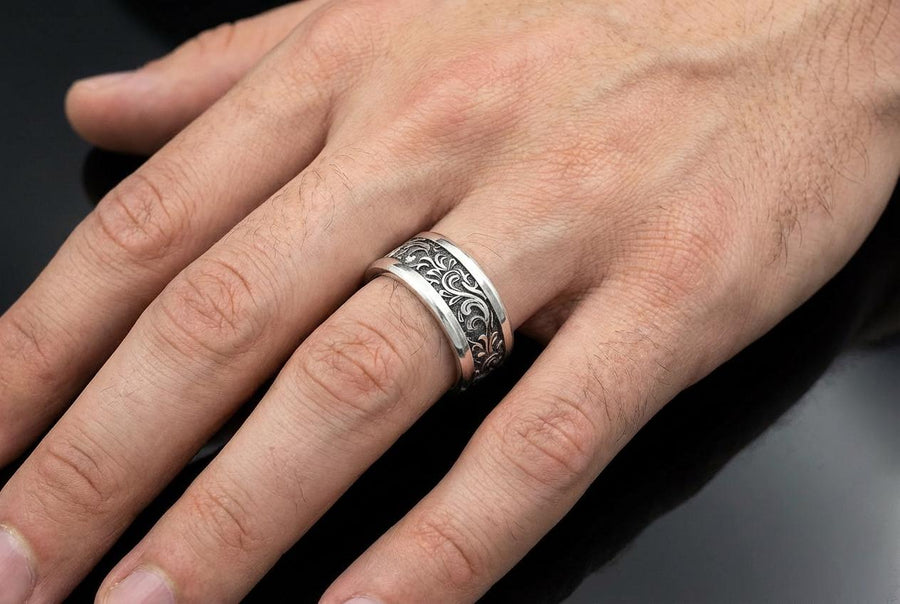 A close-up studio shot of a matching organic gothic wedding band set in sterling silver, resting on a dark, reflective surface. The rings feature a continuous, high-relief pattern of intricate sterling silver vine patterns and swirling leaves. The recessed areas are heavily oxidized to a dark matte black, creating a high-contrast shadow effect that makes the polished organic scrollwork stand out brilliantly against the dark background.
