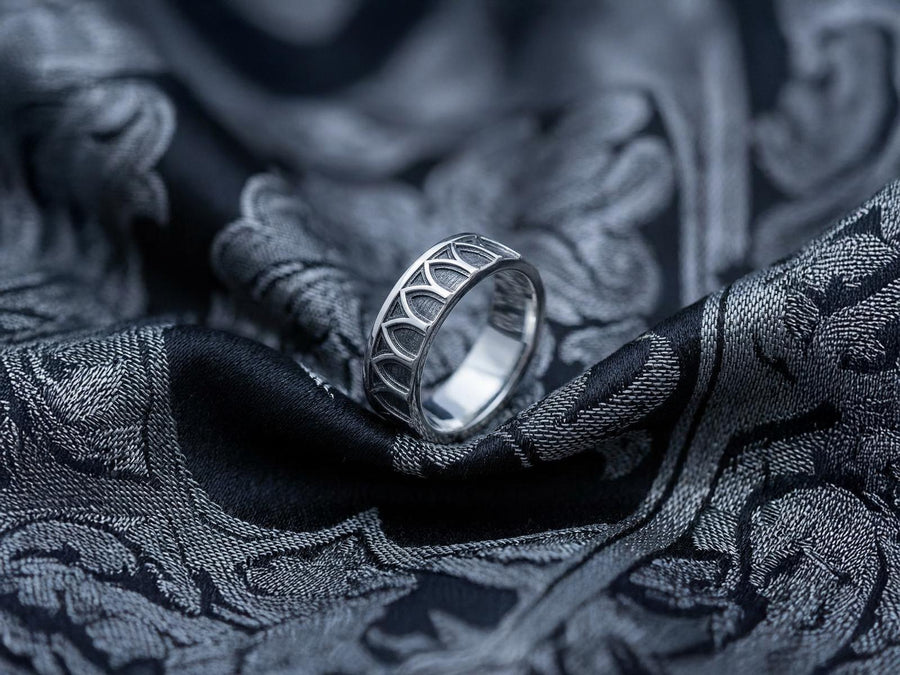 A high-resolution studio photograph of a matching sterling silver gothic wedding ring set resting on a reflective black background. The set features a wide band with a continuous arcade of pointed lancet arches. The companion engagement ring beautifully matches the arch design, forming a dramatic tiara silhouette accented by small, round black gemstones set within the structural peaks. The silver is heavily oxidized.