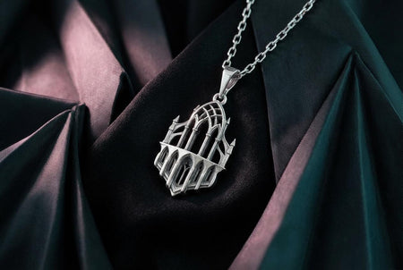 A close-up studio photograph of an intricate sterling silver pendant hanging vertically from a chain against a solid black background. The design is a highly detailed, openwork miniature of a Gothic cathedral facade or reliquary. It features a prominent central pointed lancet arch supported by slender columns, flanked by smaller matching arches and topped with sharp spires and gothic pinnacles. The polished silver highlights contrast with dark oxidation. (etsy image id: 7979028422)