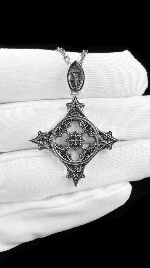 Showcasing exceptional openwork silversmithing, this gothic cross pendant demonstrates precise micro-casting techniques. The slender mullions and tracery lines are perfectly symmetrical and structurally sound, maintaining the airy lightness of a true cathedral window. A sturdy, intricately decorated silver bail is seamlessly integrated into the top point, ensuring the heavy charm hangs perfectly balanced on its chain. (etsy image id: 8027043505)