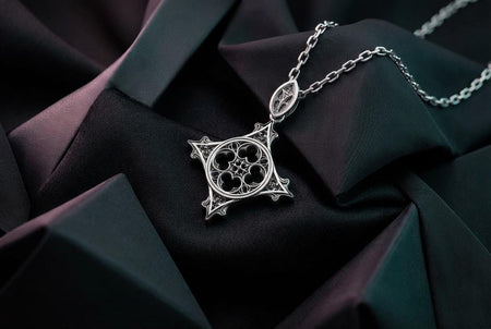 A macro studio photograph of an openwork sterling silver pendant resting on a dark surface. The design features a gothic cross-like silhouette enclosing a circular medieval quatrefoil tracery pattern. The raised silver architectural lines are highly polished, contrasting with the dark oxidized recesses to create a striking shadow-box effect that mimics stone cathedral windows. (etsy image id: 7979196412)