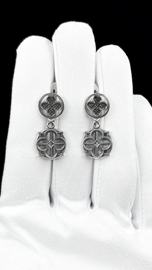 The image highlights the specific textures of the casting. The top stud has a "waffle" or lattice texture inside the quatrefoil lobes, mimicking chainmail or stone carving. The bottom drop is smooth and open, providing a visual counterweight. The 925 sterling silver is treated with an antique patina to enhance the "old world" feel. Modeled as a versatile daily earring, the "coin" size is modest enough for office wear (etsy image id: 5775868859)