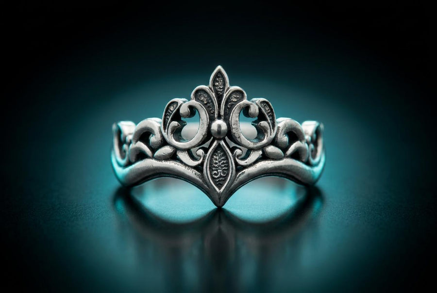A close-up studio shot of a matching sterling silver gothic wedding ring set resting on a dark reflective surface. The set includes a wide band and a matching V-shaped chevron ring that nests perfectly against it. Both rings feature raised, polished silver scrollwork and fleur-de-lis motifs set against a deeply oxidized, stippled dark grey background. The intricate relief mimics medieval stone carvings, offering a rugged yet highly sophisticated
