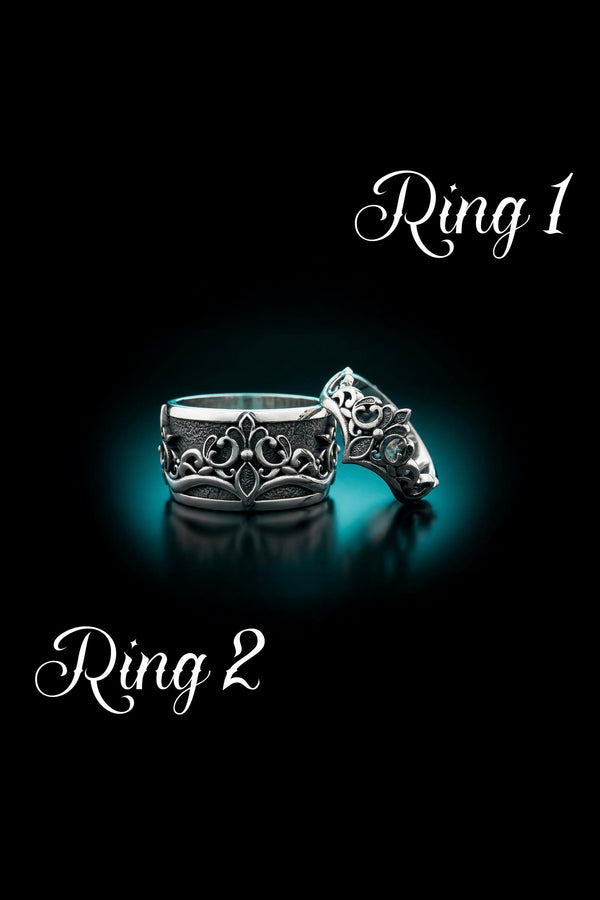 A close-up studio shot of a matching sterling silver gothic wedding ring set resting on a dark reflective surface. The set includes a wide band and a matching V-shaped chevron ring that nests perfectly against it. Both rings feature raised, polished silver scrollwork and fleur-de-lis motifs set against a deeply oxidized, stippled dark grey background. The intricate relief mimics medieval stone carvings, offering a rugged yet highly sophisticated