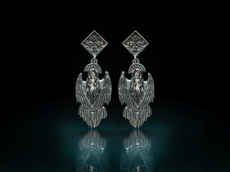 A detailed studio macro shot of a pair of articulated sterling silver earrings on a dark reflective surface. The top stud is a diamond shape enclosing a gothic floral cross. It suspends a highly detailed seraphim angel figure featuring a faceless head crowned with a studded halo. Her large, textured wings fold downwards into a feathered skirt. The silver is oxidized, leaving the recesses dark while the raised feathers gleam. (etsy image id: 8003029872)