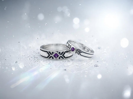 A close-up studio shot of a matching sterling silver minimalist gothic wedding ring set on a black reflective surface. The set features a wide men's band and a slightly narrower women's engagement ring. Both feature a repeating geometric ornament of polished silver sweeping lines against a dark, oxidized stippled background. The engagement ring centers a square-cut purple amethyst set in a diamond shape.