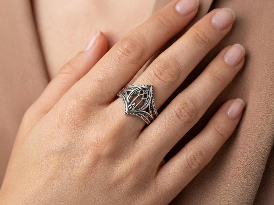 A high-resolution macro shot of a wide sterling silver wedding band resting on a sparkling, icy white surface. The ring features an intricate openwork design mimicking a Gothic cathedral window, complete with pointed lancet arches and delicate stone tracery. The polished silver highlights contrast beautifully against the dark, oxidized background, emphasizing the architectural depth of the piece.