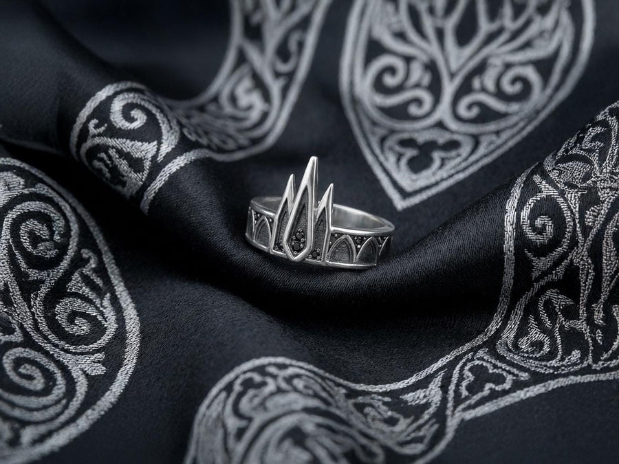 A high-resolution studio photograph of a matching sterling silver gothic wedding ring set resting on a reflective black background. The set features a wide band with a continuous arcade of pointed lancet arches. The companion engagement ring beautifully matches the arch design, forming a dramatic tiara silhouette accented by small, round black gemstones set within the structural peaks. The silver is heavily oxidized.