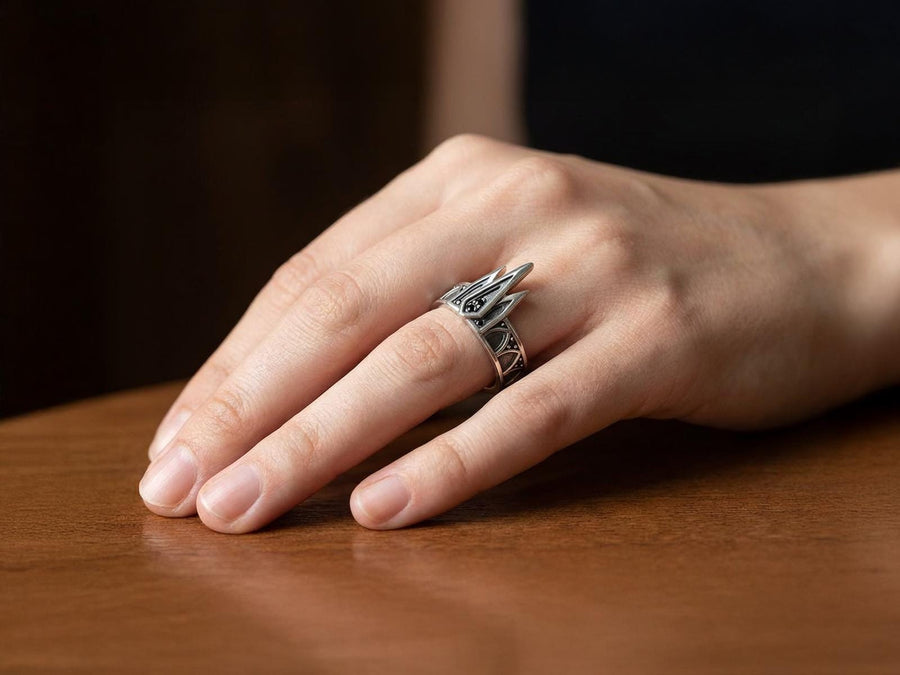 A high-resolution studio photograph of a matching sterling silver gothic wedding ring set resting on a reflective black background. The set features a wide band with a continuous arcade of pointed lancet arches. The companion engagement ring beautifully matches the arch design, forming a dramatic tiara silhouette accented by small, round black gemstones set within the structural peaks. The silver is heavily oxidized.