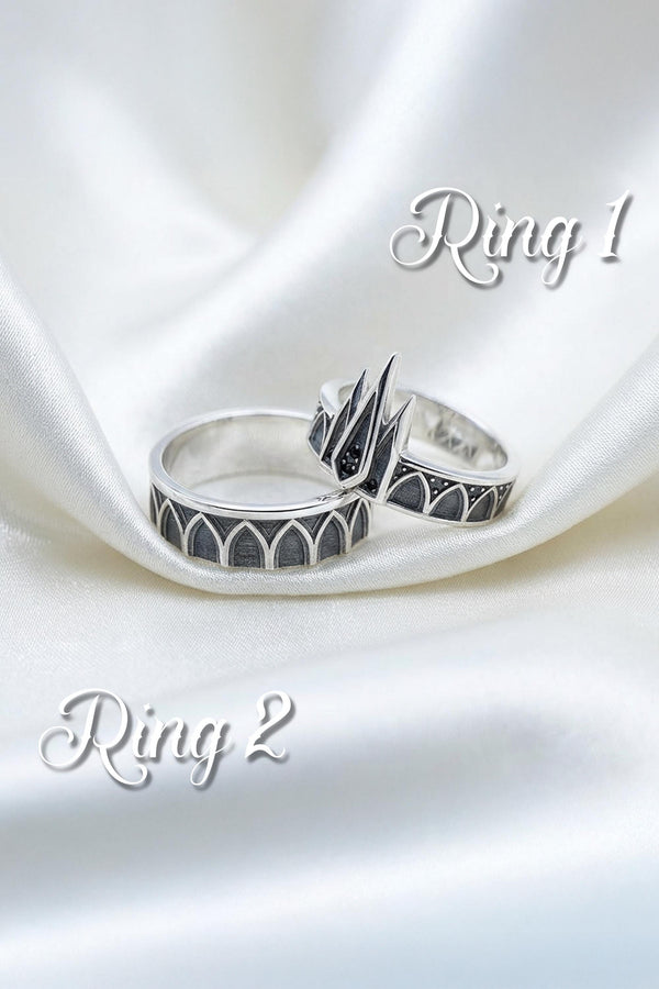 A high-resolution studio photograph of a matching sterling silver gothic wedding ring set resting on a reflective black background. The set features a wide band with a continuous arcade of pointed lancet arches. The companion engagement ring beautifully matches the arch design, forming a dramatic tiara silhouette accented by small, round black gemstones set within the structural peaks. The silver is heavily oxidized.