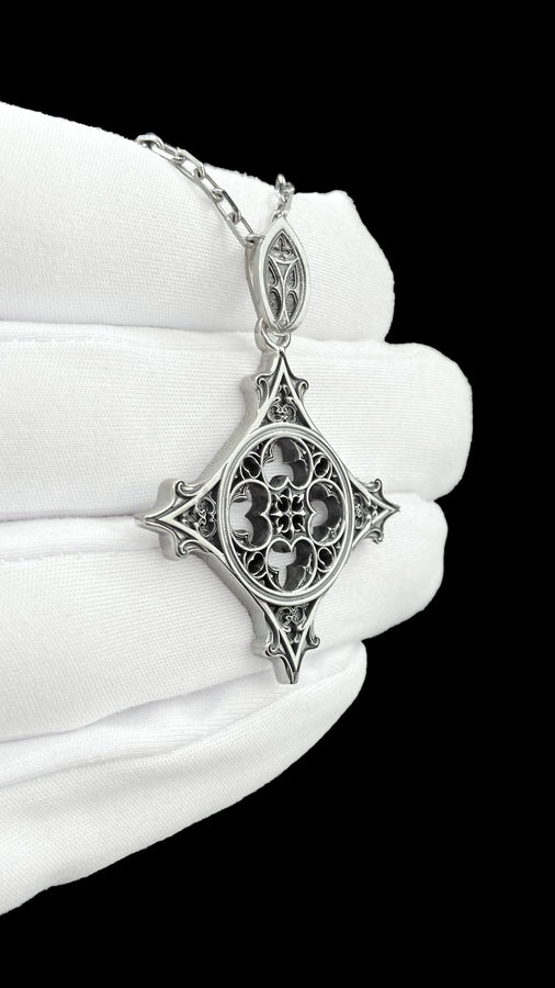 Showcasing exceptional openwork silversmithing, this gothic cross pendant demonstrates precise micro-casting techniques. The slender mullions and tracery lines are perfectly symmetrical and structurally sound, maintaining the airy lightness of a true cathedral window. A sturdy, intricately decorated silver bail is seamlessly integrated into the top point, ensuring the heavy charm hangs perfectly balanced on its chain. (etsy image id: 8027043505)