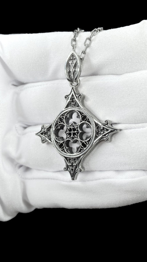 Showcasing exceptional openwork silversmithing, this gothic cross pendant demonstrates precise micro-casting techniques. The slender mullions and tracery lines are perfectly symmetrical and structurally sound, maintaining the airy lightness of a true cathedral window. A sturdy, intricately decorated silver bail is seamlessly integrated into the top point, ensuring the heavy charm hangs perfectly balanced on its chain. (etsy image id: 8027043505)