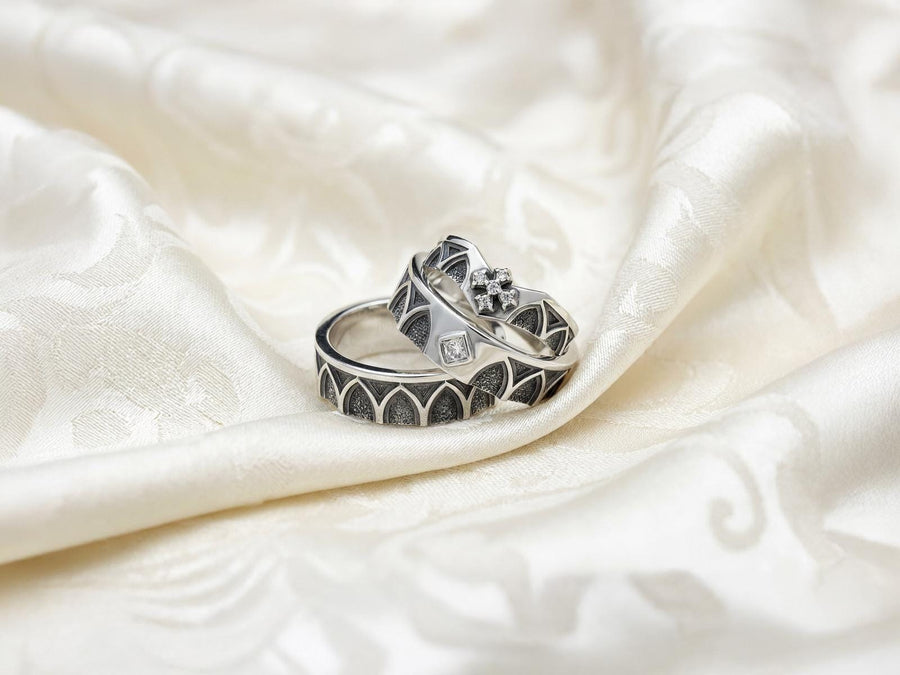 A professional studio photograph of a matching two-piece sterling silver wedding ring set. Both rings feature a prominent, raised Greek-style cross motif in the center, which holds a round, bezel-set white crystal. The interior of the cross arms has a fine, cross-hatched grid texture. Along the sides of the high-polished silver bands are recessed, four-lobed quatrefoil shapes. The rings are presented against a pitch-black background, making the p __etsy:8051335185