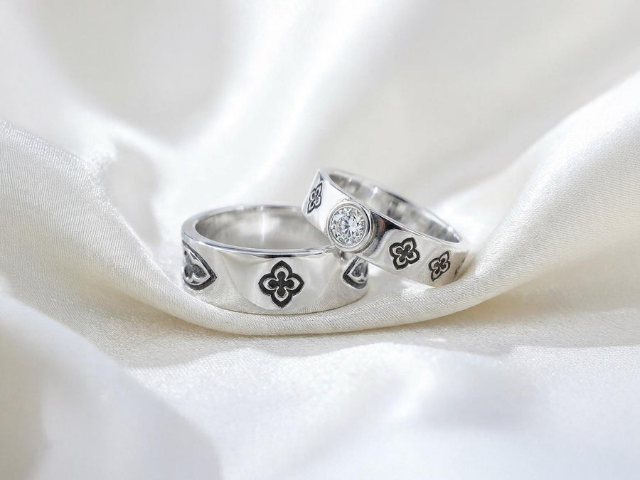 This dark academic ring set captures the mysterious romance of a medieval cathedral. Bright studio lighting highlights the polished silver rims, contrasting dramatically with the pitch-black sulfur oxidation in the carved quatrefoil recesses. Rich in gothic symbolism, the continuous quatrefoil motif represents the intersection of earth and heaven, mirroring the windows of ancient cathedrals. It serves as a profound talisman of eternal devotion an