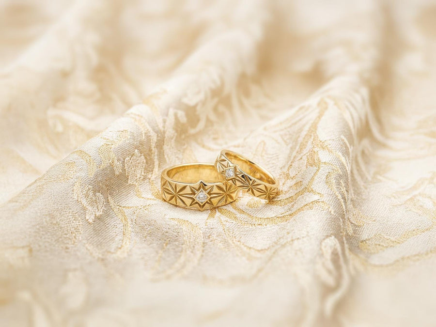 A close-up studio photograph of a matching pair of 925 sterling silver wedding bands resting on a bright, reflective white surface scattered with tiny crystals. The rings feature a continuous, deeply engraved pattern of geometric starbursts or celestial stars with radiating lines. The primary band has a square, princess-cut light blue gemstone, likely blue topaz or aquamarine, bezel-set directly into the center of the prominent front-facing star.