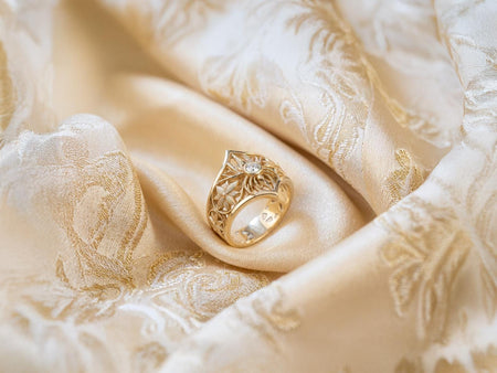 Reimagined in solid 18k yellow gold, this architectural Arachne ring transforms into an opulent royal treasure from an ancient court. The warm golden metal makes the central spider and ornate window frame glow like a sunlit relic, while the black onyx stone creates a magnificent contrast of pure luxury. A soft, brushed matte finish in the recesses replaces the oxidation, allowing the geometric rosettes to shimmer with a classic, sophisticated lus