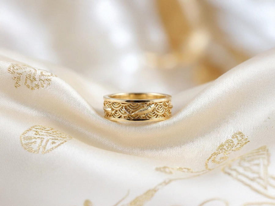 A close-up studio photograph of a matching pair of 925 sterling silver wedding bands resting on a bright, reflective surface scattered with water droplets or ice crystals. The rings feature a deeply engraved, continuous pattern of traditional Japanese Seigaiha ocean waves. Overlaid on the wave texture are sculpted, three-dimensional koi fish swimming elegantly along the curved bands. The recessed areas of the silver are deeply oxidized to a dark
