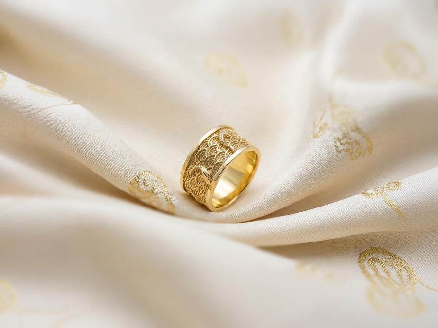 A close-up studio photograph of a matching pair of 925 sterling silver wedding bands resting on a bright, reflective surface scattered with water droplets or ice crystals. The rings feature a deeply engraved, continuous pattern of traditional Japanese Seigaiha ocean waves. Overlaid on the wave texture are sculpted, three-dimensional koi fish swimming elegantly along the curved bands. The recessed areas of the silver are deeply oxidized to a dark