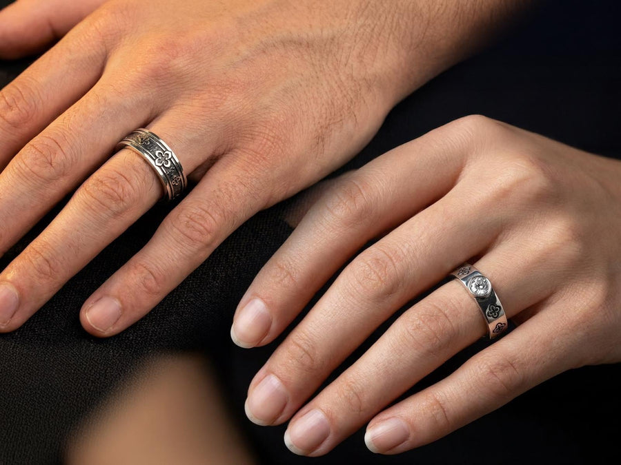 This dark academic ring set captures the mysterious romance of a medieval cathedral. Bright studio lighting highlights the polished silver rims, contrasting dramatically with the pitch-black sulfur oxidation in the carved quatrefoil recesses. Rich in gothic symbolism, the continuous quatrefoil motif represents the intersection of earth and heaven, mirroring the windows of ancient cathedrals. It serves as a profound talisman of eternal devotion an