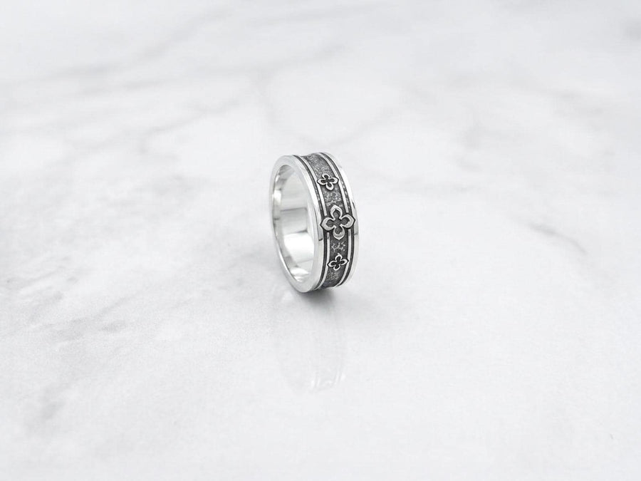 This dark academic ring set captures the mysterious romance of a medieval cathedral. Bright studio lighting highlights the polished silver rims, contrasting dramatically with the pitch-black sulfur oxidation in the carved quatrefoil recesses. Rich in gothic symbolism, the continuous quatrefoil motif represents the intersection of earth and heaven, mirroring the windows of ancient cathedrals. It serves as a profound talisman of eternal devotion an