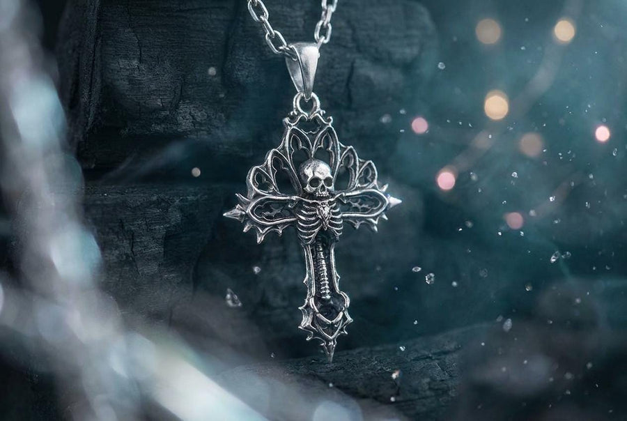 A close-up studio photograph of a 925 sterling silver gothic cross pendant resting on a light, finely textured surface. The core of the cross features a detailed skull, ribcage, and a spine extending down the bottom arm. The upper arms are crafted with openwork medieval tracery resembling cathedral windows. The recessed silver is heavily oxidized to a dark gray, contrasting sharply with the polished bone and architectural highlights.