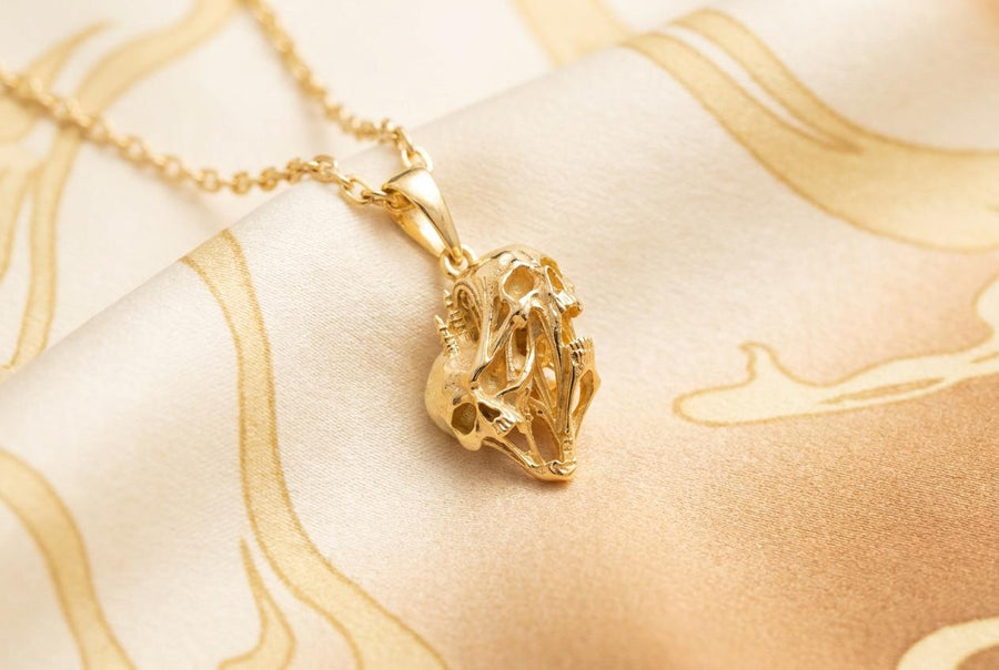 A side-profile view of the silver skull pendant showcases the breathtaking depth of the sculpted elements. The skulls appear stretched and elongated, morphing into each other. Dark oxidation heavily shadows the deeply recessed areas of the bone.