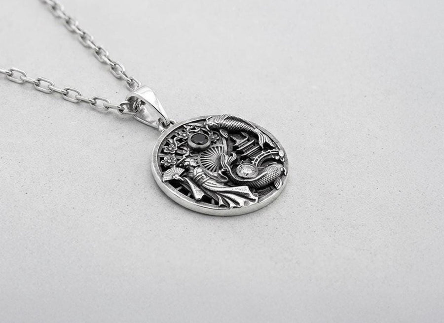 Crafted from solid 925 sterling silver, this intricate medallion demonstrates the visual impact of an antiqued patina. The heavy oxidation settles into the carved pagoda and the detailed scales of the koi fish. A dark black onyx and a sparkling clear gemstone add striking contrast to the silver.