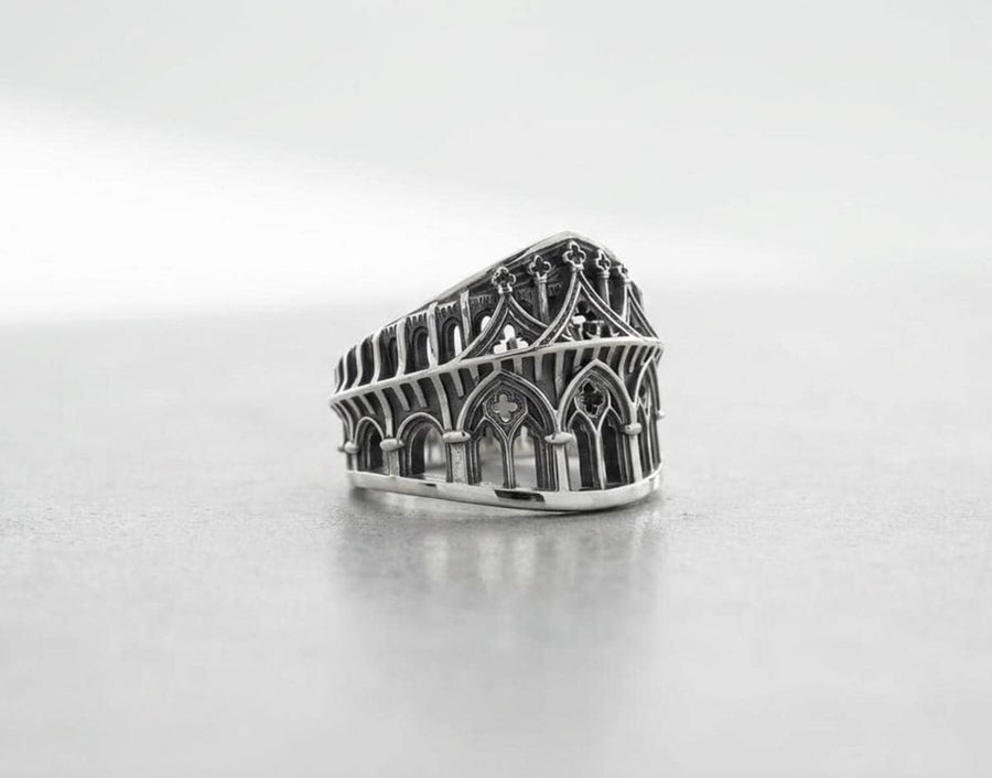 This striking artisan ring perfectly captures the monumental scale of medieval architecture. Bright studio lighting illuminates the polished silver arches and columns, contrasting beautifully with the deep, dark oxidation inside the hollow windows and recesses. Crafted from premium solid 925 sterling silver, this wide architectural band demonstrates the visual impact of an antiqued patina. Heavy sulfur oxidation settles into the intricate crevice