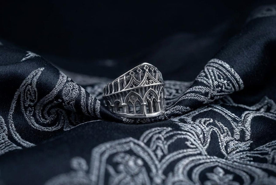 This striking artisan ring perfectly captures the monumental scale of medieval architecture. Bright studio lighting illuminates the polished silver arches and columns, contrasting beautifully with the deep, dark oxidation inside the hollow windows and recesses. Crafted from premium solid 925 sterling silver, this wide architectural band demonstrates the visual impact of an antiqued patina. Heavy sulfur oxidation settles into the intricate crevice