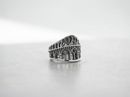 This striking artisan ring perfectly captures the monumental scale of medieval architecture. Bright studio lighting illuminates the polished silver arches and columns, contrasting beautifully with the deep, dark oxidation inside the hollow windows and recesses. Crafted from premium solid 925 sterling silver, this wide architectural band demonstrates the visual impact of an antiqued patina. Heavy sulfur oxidation settles into the intricate crevice